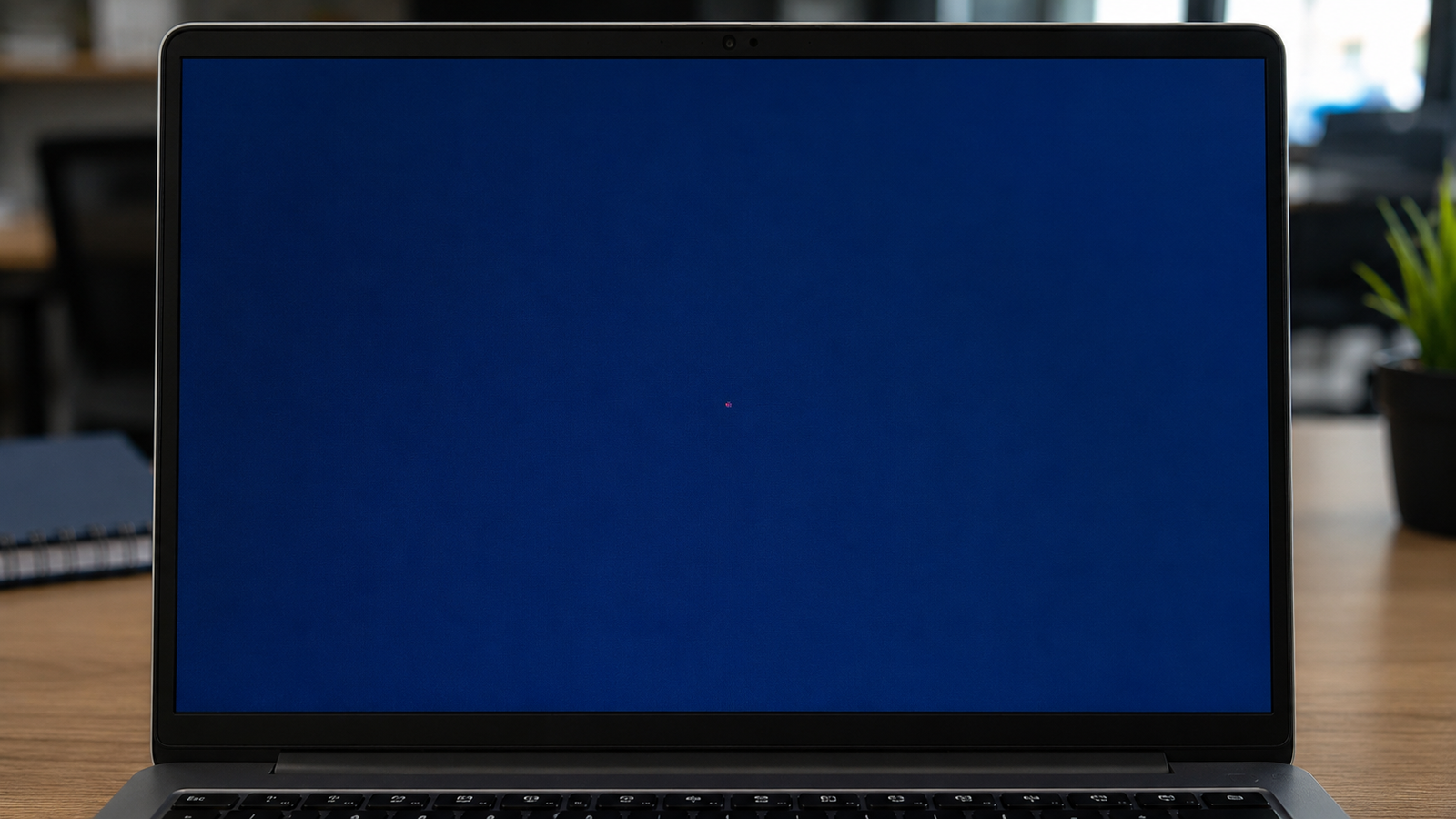 Close-up of a dead pixel visible as a single bright dot on a laptop screen displaying a solid blue background